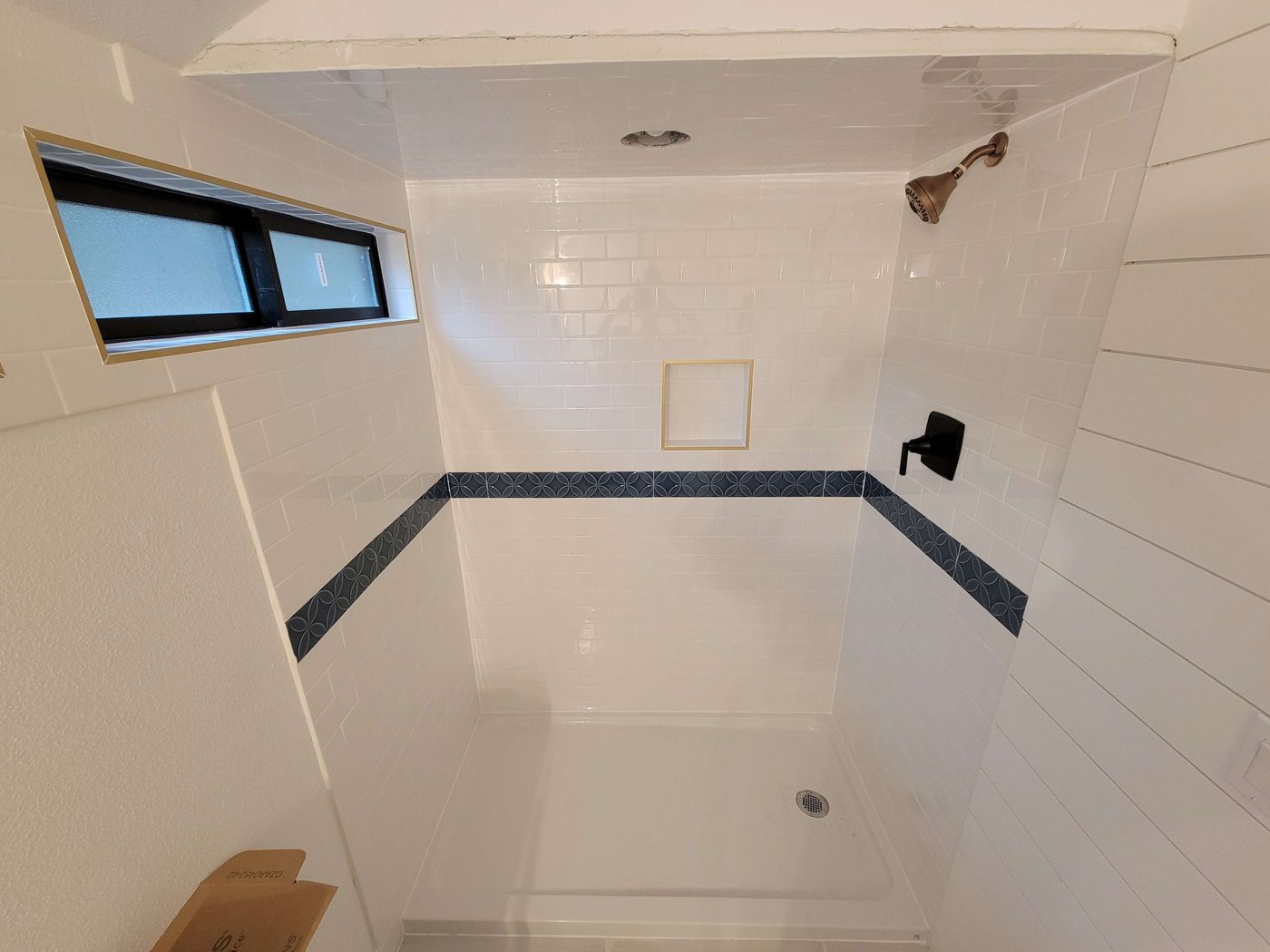 Remodeled bathroom shower with white subway tile and a patterned accent band